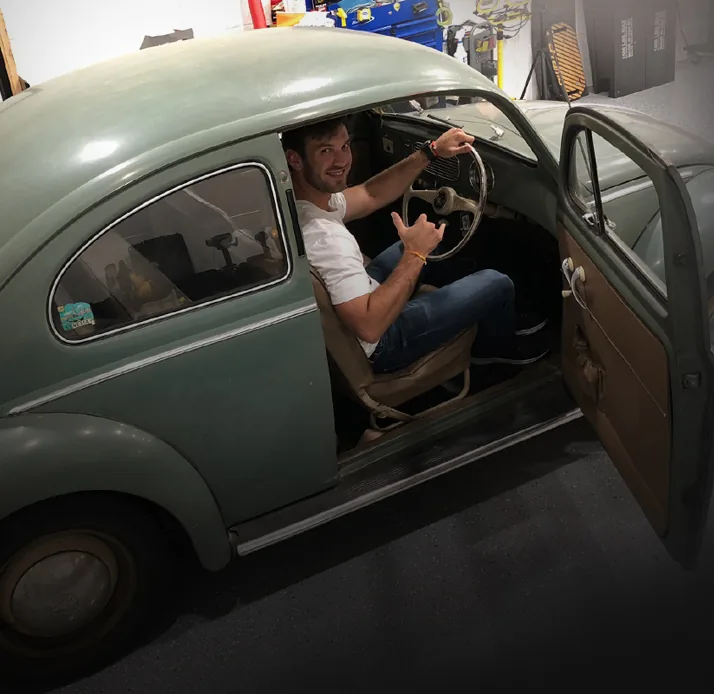 Daniel Suárez sitting in a classic Volkswagen Beetle in his workshop